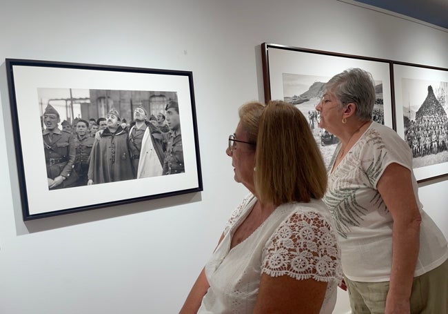 Dos mujeres observan, en la muestra inaugurada en Alhaurín de la Torre, la famosa fotografía que Bartolomé Ros tomó a Franco y Millán Astray, abrazados, mientras entonaban cánticos legionarios.
